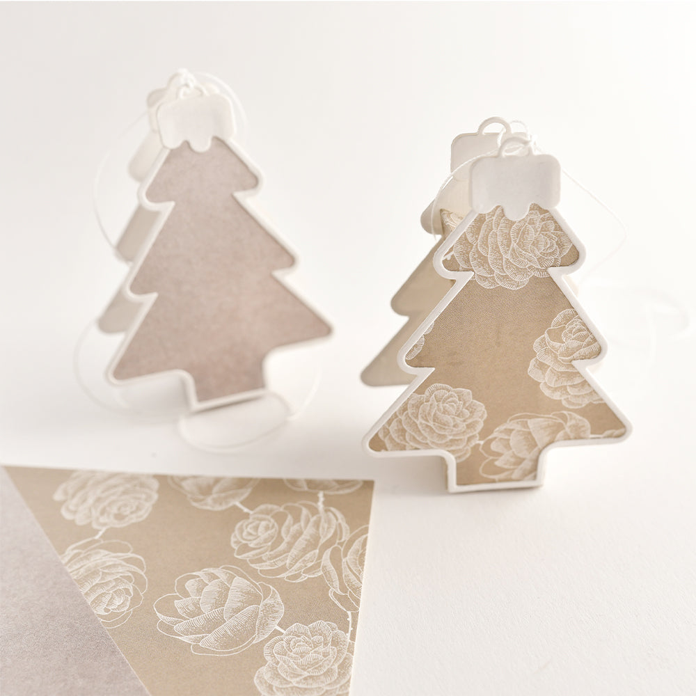 Zwei Weihnachtsbaumschmuckstücke aus Papier mit einem weißen Blumenmotiv, das mit Stanzsystemen hergestellt wurde.