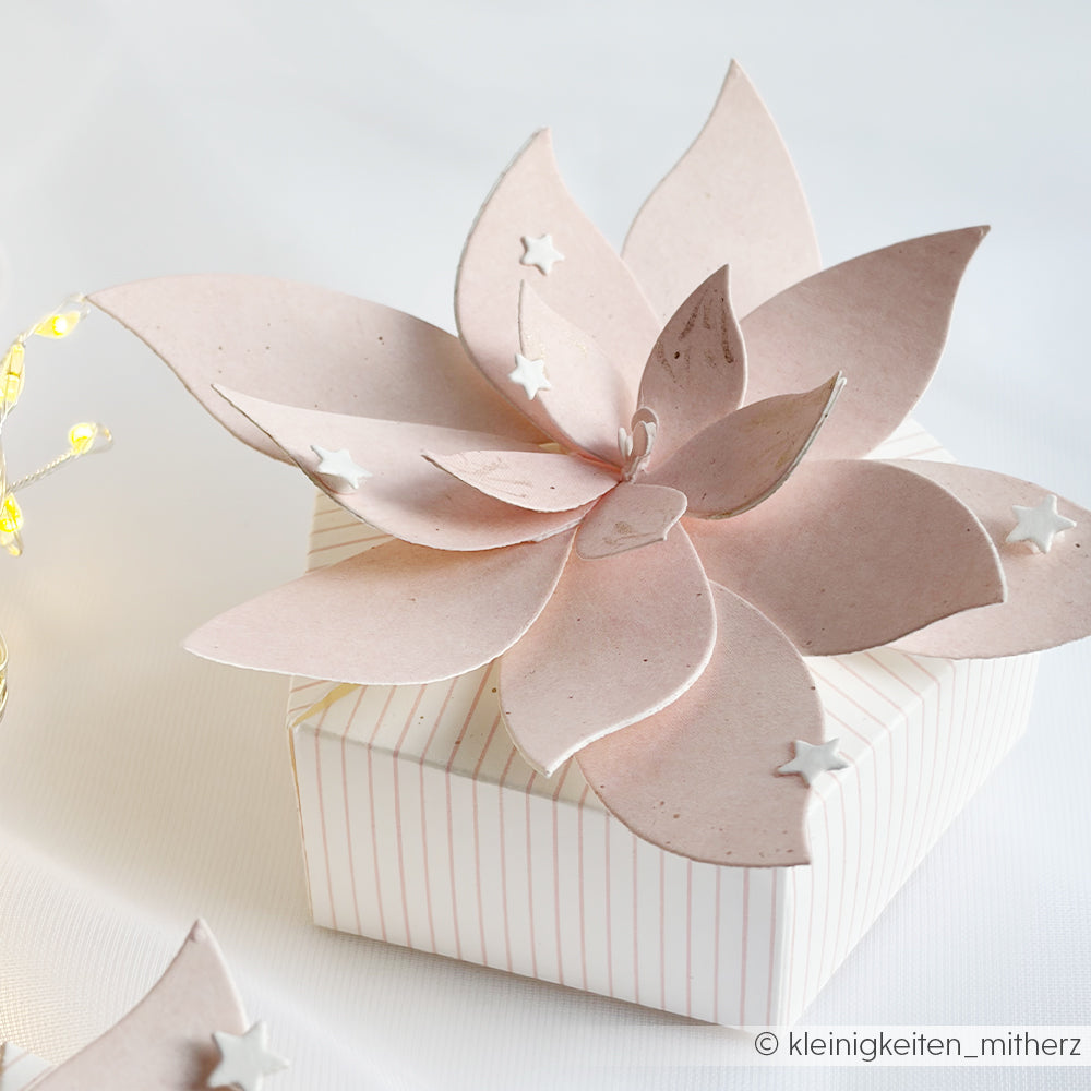 Kleine Geschenkbox mit einer großen, hellrosa Papierblume und Sternverzierungen, die mit der Motivstanze gestaltet wurden.