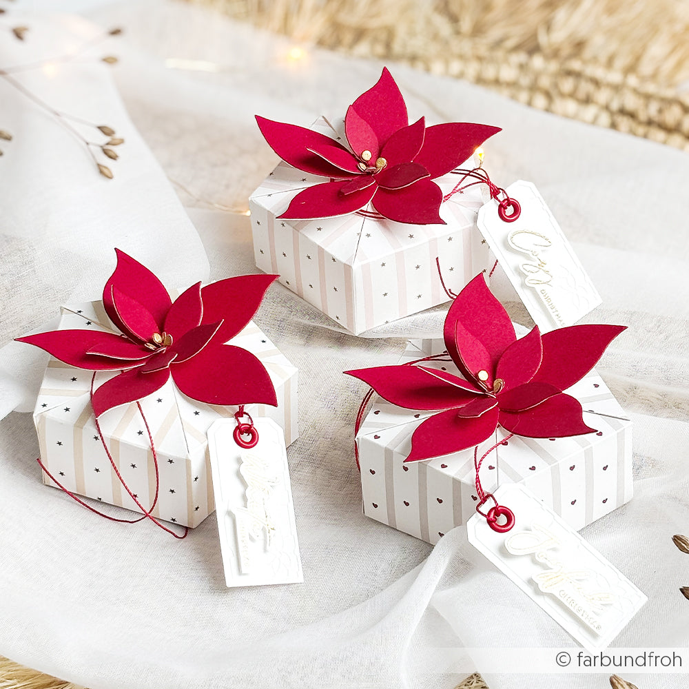 Drei kleine Geschenkboxen, verziert mit roten Weihnachtssternen aus „Motivstanze“-Papier und weißen Weihnachtsanhängern.