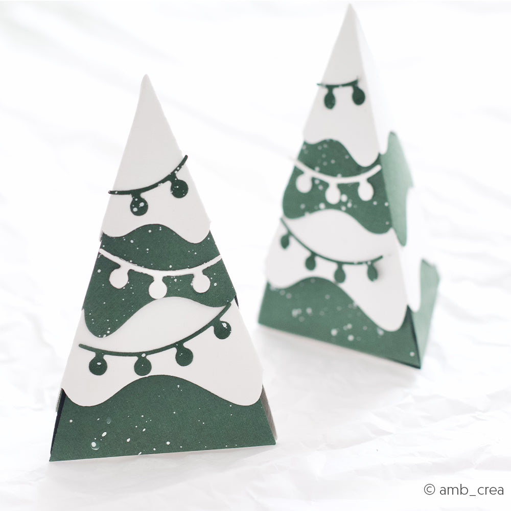 Zwei dreieckige Weihnachtsbaum-Geschenkboxen aus Designpapier mit Lichterkette.