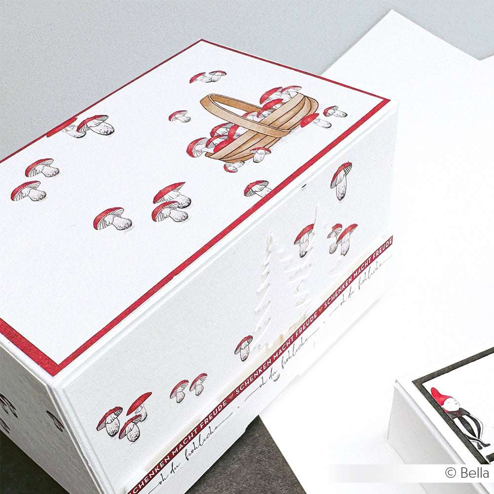 Bezaubernde weiße Schachtel von Alexandra Renke mit rotem Deckel und handgezeichneten Illustrationen von Pilzen und Holzschlitten - ein einzigartiger Designpapier-Akzent, der sich perfekt für Grußkarten oder besondere handgemachte Geschenke eignet.
