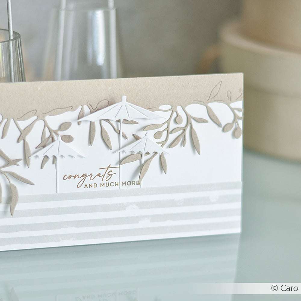 Handgefertigte Karte mit Blattausschnitten, die mit Alexandra Renke Stanzformen hergestellt wurden, einem gestreiften Muster und einer eleganten Schrift, die u. a. "Glückwünsche" sagt.