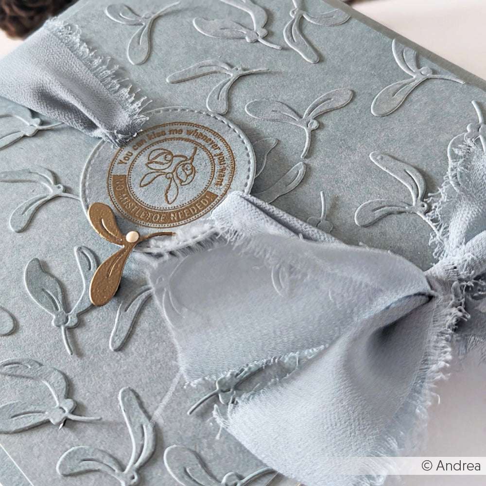 Hellblaue Prägekarte von Vivant Decorations BV mit Mistelmuster, ausgefranstem Chiffonband und einem goldenen Siegel - ideal für winterliche Bastelprojekte und festliche Deko Ideen.