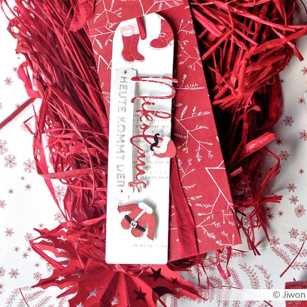 Das weihnachtliche Lesezeichen von Alexandra Renke zeigt ein Weihnachtsmannkostüm mit Mütze und Stiefeln auf rotem Designpapier, gepaart mit einem festlichen roten Umschlag.