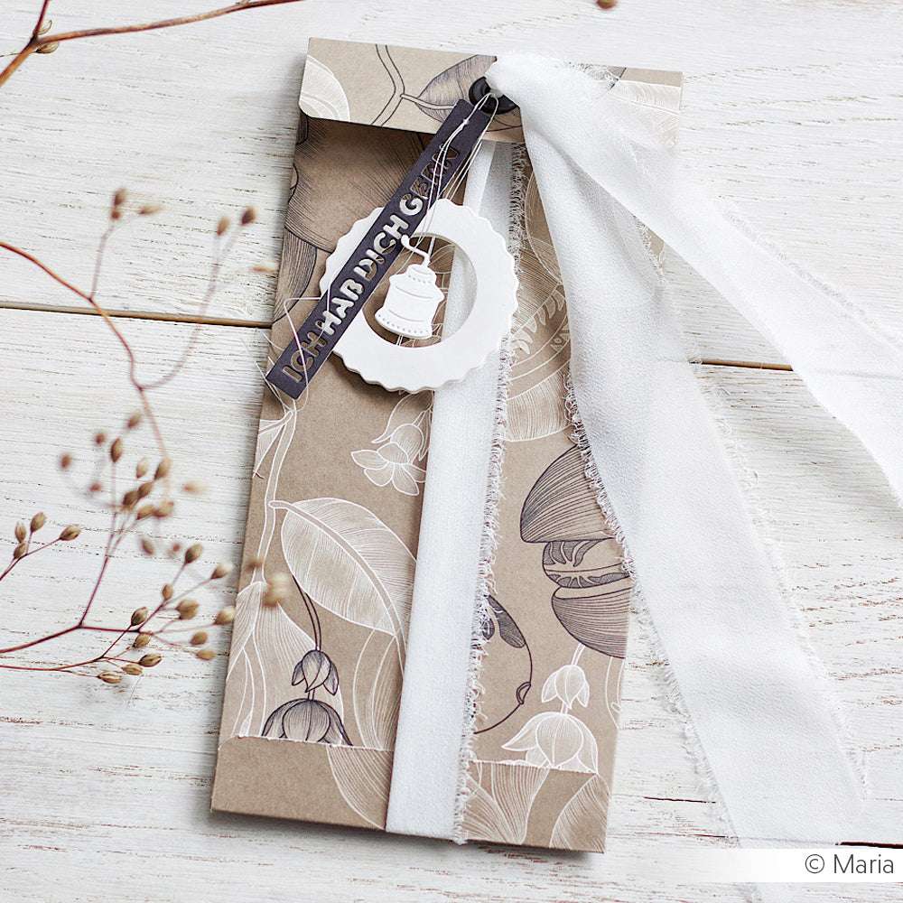 Hellbrauner, geblümter Umschlag von Alexandra Renke, gefertigt aus Designpapier mit weißem Band, kreisförmigem Anhänger und "Von Hand gemacht"-Etikett auf weißer Holzoberfläche. Perfekt für Papierprojekte und Buchbinderei-Kreationen.