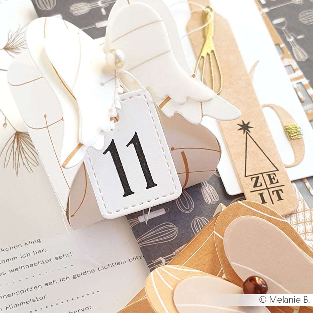 Engelchen-Papierbastelei von Alexandra Renke mit einem klaren Stempelanhänger mit der Nummer 11, akzentuiert durch neutrale und goldene Dekorationen.
