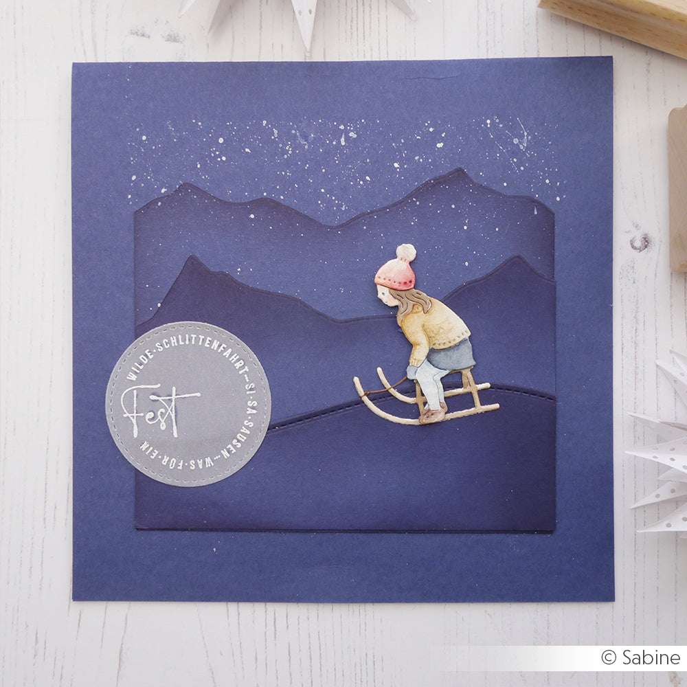 Handgefertigte Karte von Alexandra Renke mit einem Schlittenkinder-Mädchen, das nachts über verschneite Hügel schlittert, mit lilafarbenen Bergen, Sternen und eleganten Designpapiere-Akzenten.