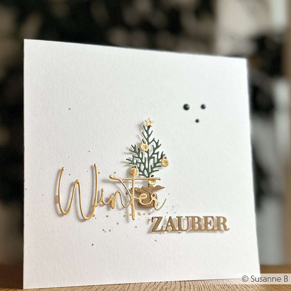 Weiße Karte von Alexandra Renke mit dem Text "Winter ZAUBER", einem kleinen 3D-Weihnachtsbaum, der mit DieCut Systemen hergestellt wurde, und goldenen Akzenten auf der Vorderseite.