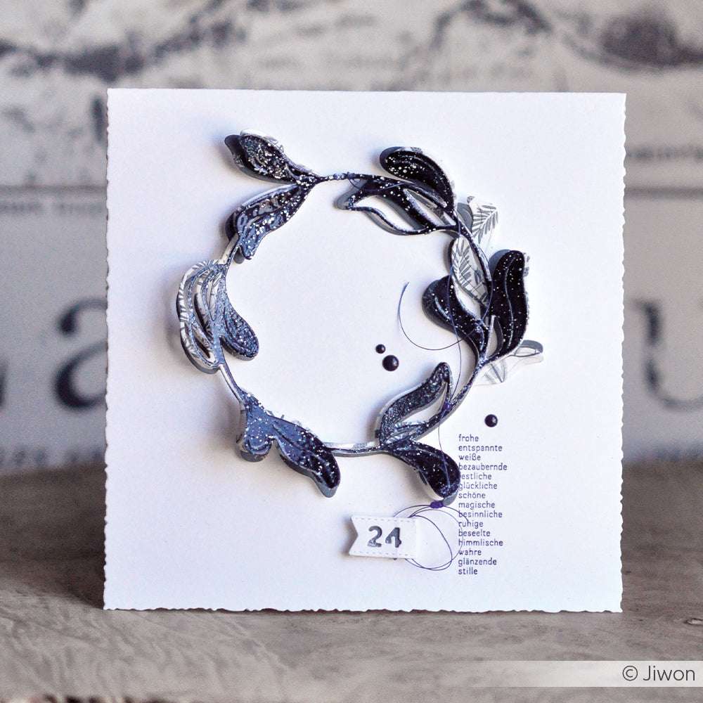 Eine weiße Karte von Alexandra Renke mit einem silber-schwarzen Kranz, der Zahl 24, kleinen deutschen Wörtern darunter und zarten Details aus Motivstanze Dies.