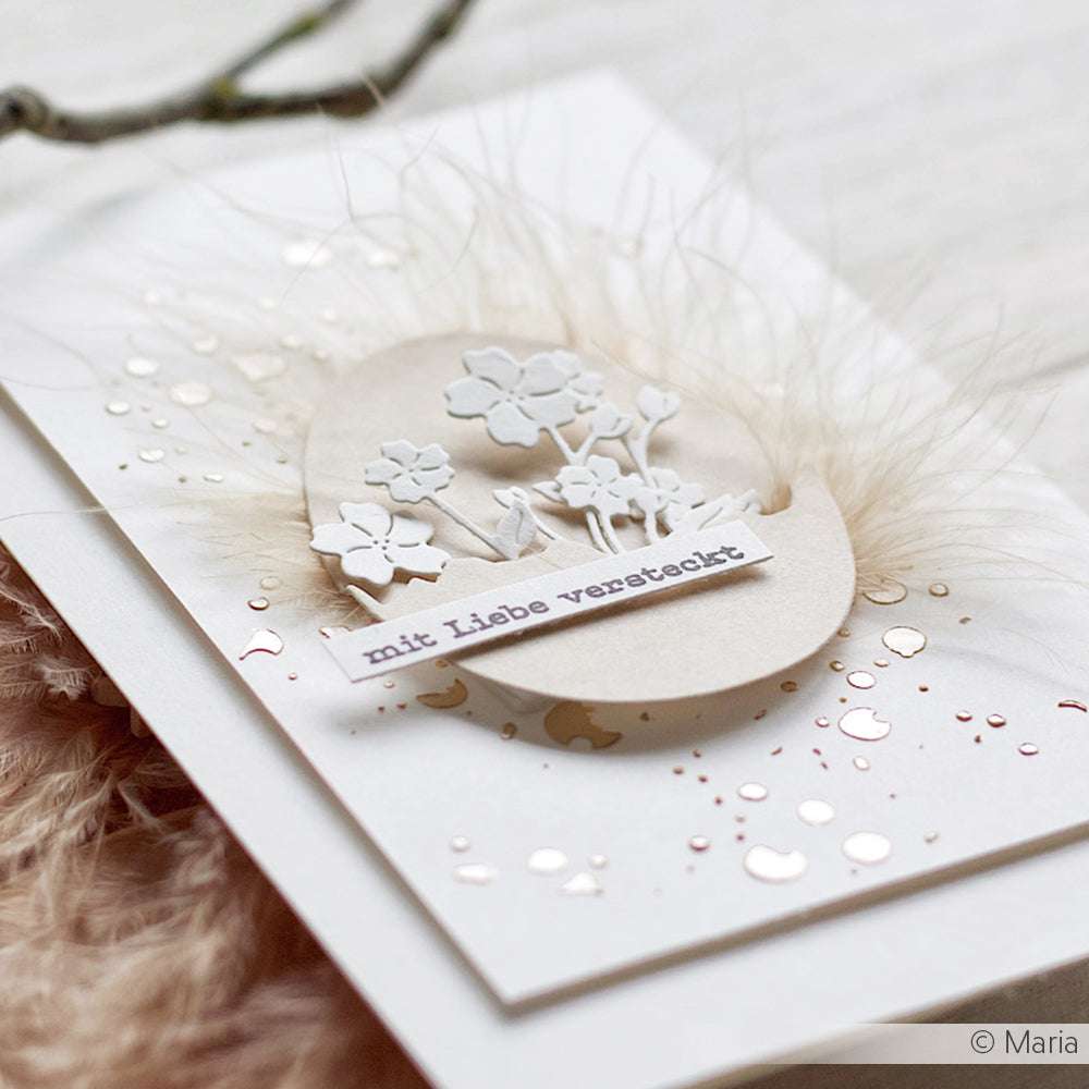 Eine zarte handgefertigte Karte von ☆ mit Blumenausschnitten, Federn und dem deutschen Text "mit Liebe versteckt", veredelt mit schimmernder Roségoldfolie.