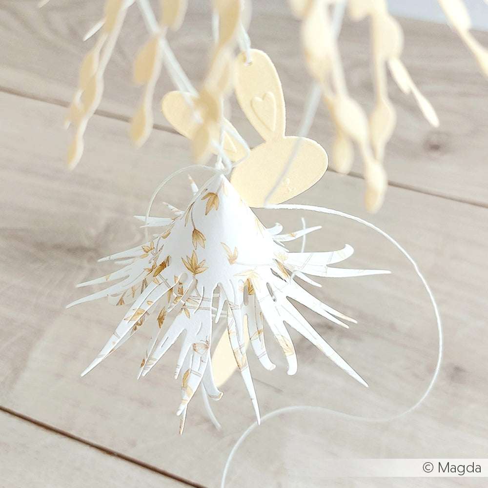 Eine weiß-goldene Papierblume mit Stacheln, die von Alexandra Renke Designpapiere hergestellt wurde, hängt an einer Schnur auf einer Holzoberfläche.