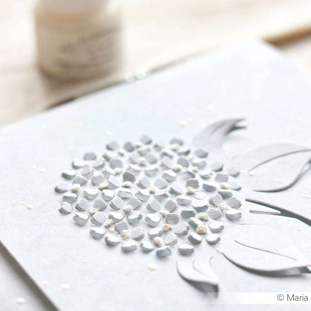 Nahaufnahme einer strukturierten weißen Papierkarte mit erhabenen Blumenmustern und ausgeschnittenen Blättern, hergestellt mit der säurefreien, wasserbasierten Allzweck-Pigmenttinte von Tsukineko für dauerhafte Schönheit.