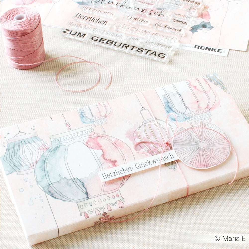 Das Geschenk wurde mit pastellfarbenem Papier mit Laternenmotiven von Alexandra Renke, rosa Makramee-Schnur und einem "Herzlichen Glückwunsch"-Anhänger verpackt.