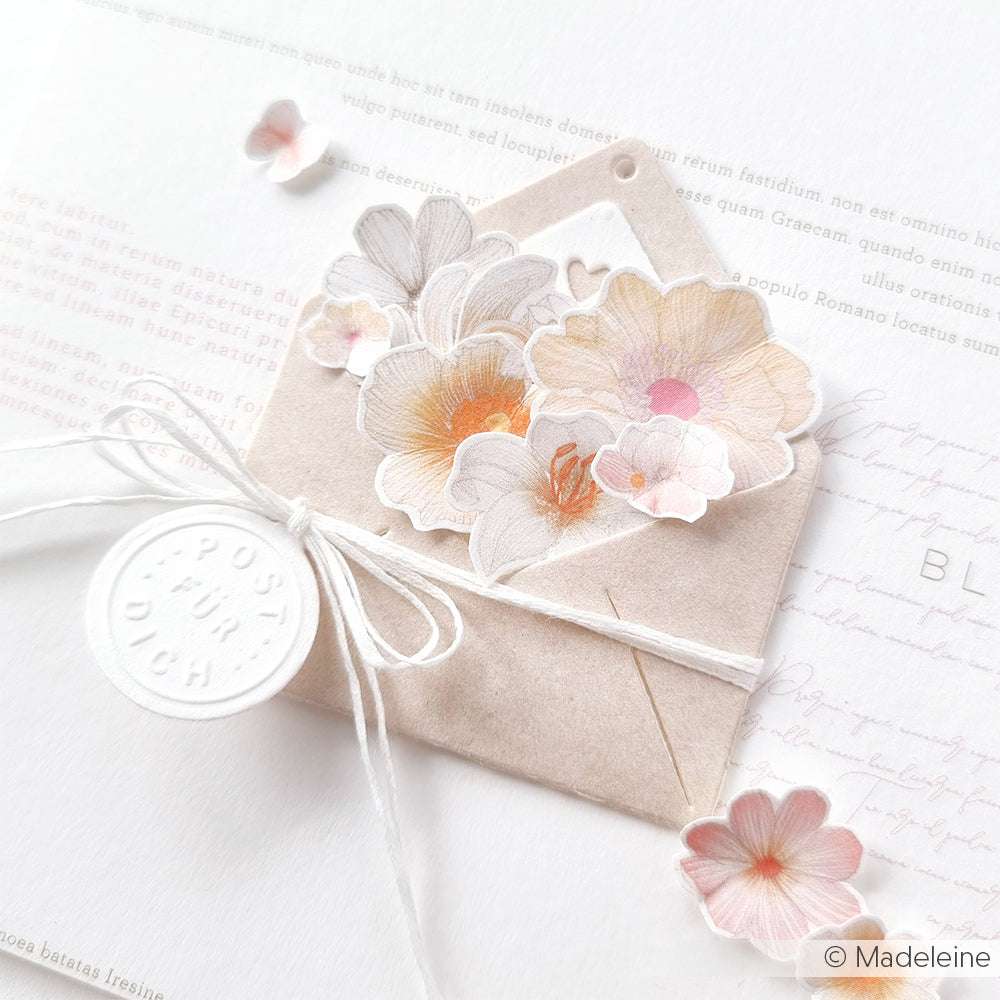 Ein kleiner Umschlag mit zarten pastellfarbenen Blumenausschnitten aus Alexandra Renkes Motivstanze, weißem Garn und einem runden Prägestempel auf einem Brief.
