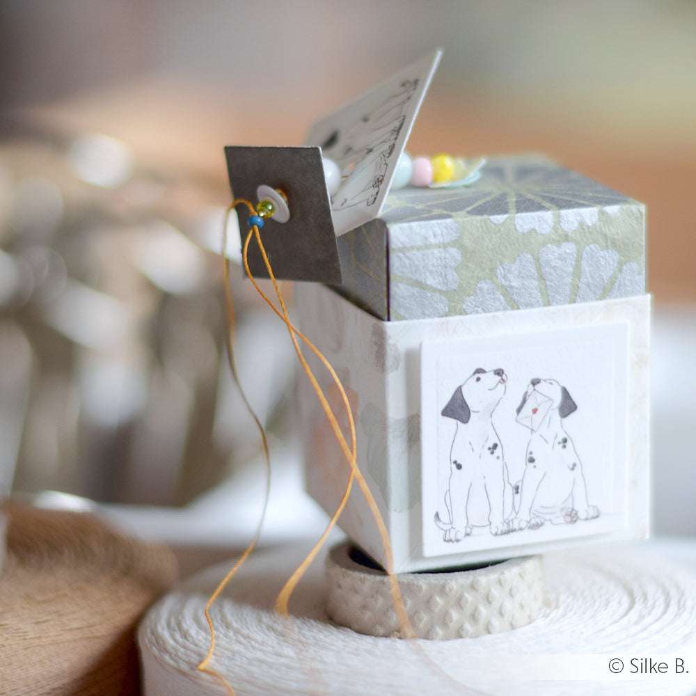 Dekorative Dose von Alexandra Renke mit einer Zeichnung von zwei Dalmatinerwelpen, einem offenen Deckel und gelben Makramee-Fäden.