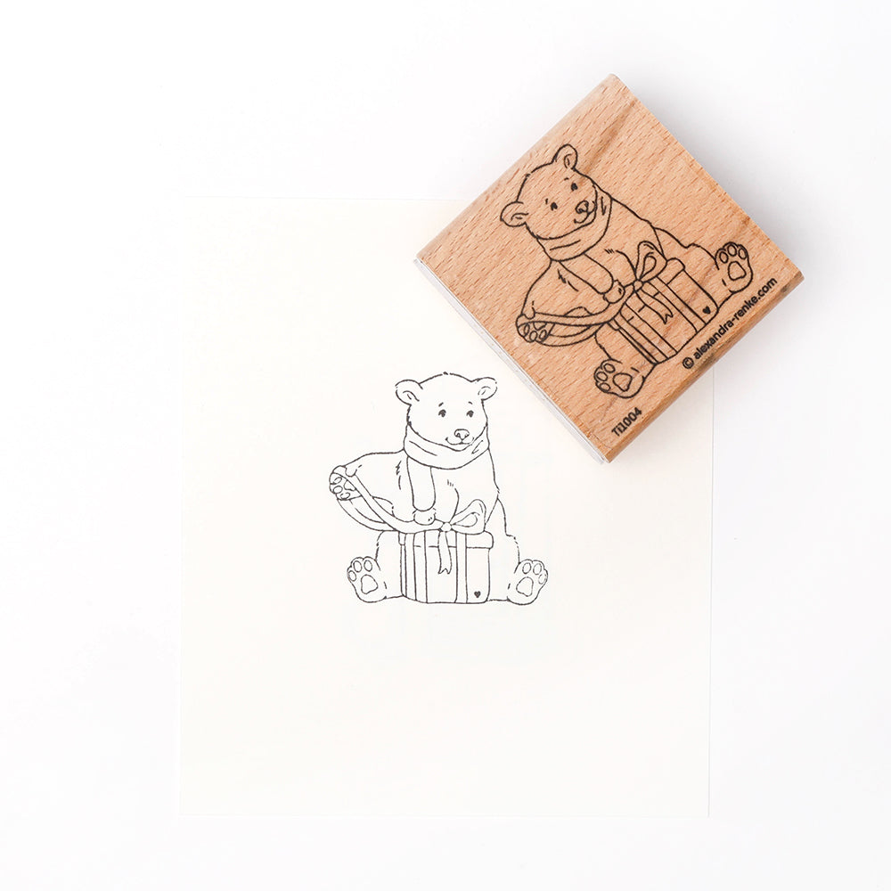 Eine Holzbriefmarke von Alexandra Renke mit einem Aufdruck des kleinen Eisbären Boris, der in einer verpackten Geschenkbox sitzt.
