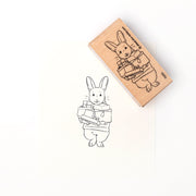 Ein gestempelter Umriss von Hase Henry, der Geschenke trägt, neben dem Alexandra Renke Holzstempel, mit dem dieses bezaubernde Stempelmotiv gestaltet wurde.