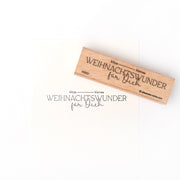Ein Holzstempel und Stempelkissen von Alexandra Renke hinterlassen den Schriftzug "Kitzekleines Weihnachtswunder für Dich" auf weißem Papier.