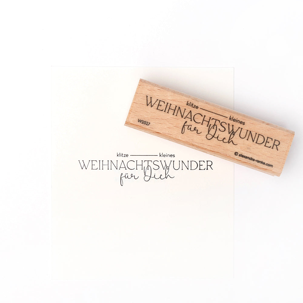 Ein Holzstempel und Stempelkissen von Alexandra Renke hinterlassen den Schriftzug "Kitzekleines Weihnachtswunder für Dich" auf weißem Papier.