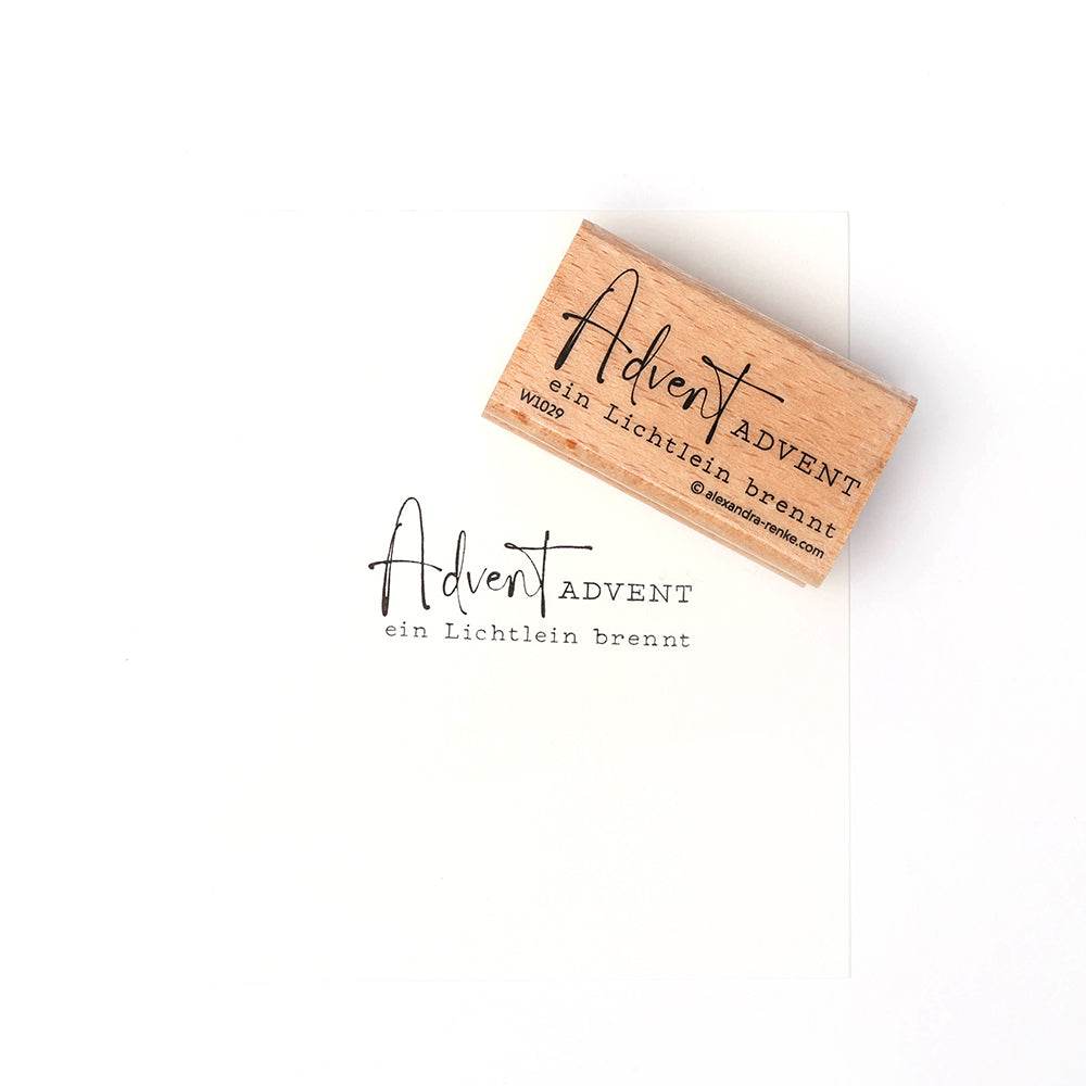 Ein Holzstempel von Alexandra Renke mit dem Text "Advent Advent ein Lichtlein brennt" ist auf weißem Papier gestempelt, daneben liegt das Stempelkissen.
