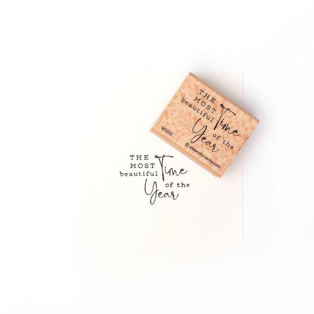 Ein Holzstempel von Alexandra Renke und Papier mit der Aufschrift "Die schönste Zeit des Jahres" in gemischten Schriftarten - ideal für Papierprojekte oder in Kombination mit Ihren Lieblingsstempelkissen.