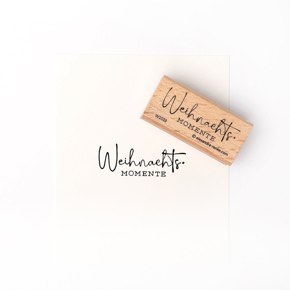 Ein Holzstempel von Alexandra Renke mit dem Schriftzug "Weihnachts MOMENTE" verleiht jedem Papier stilvolle festliche Akzente.