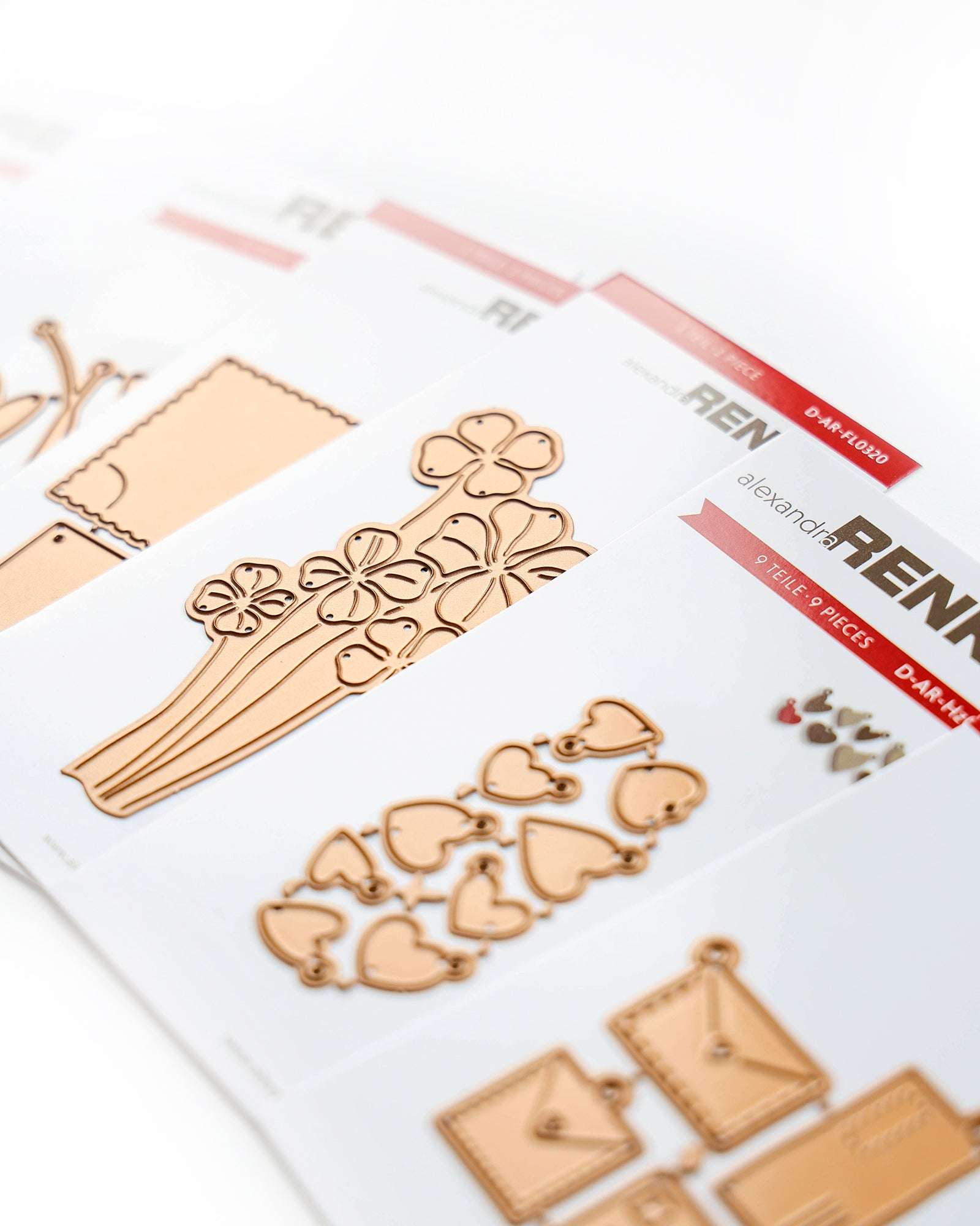 Metallische Stanzschablonen zum Basteln mit Blumen-, Herz- und Umschlagmotiven auf weißen Karten.