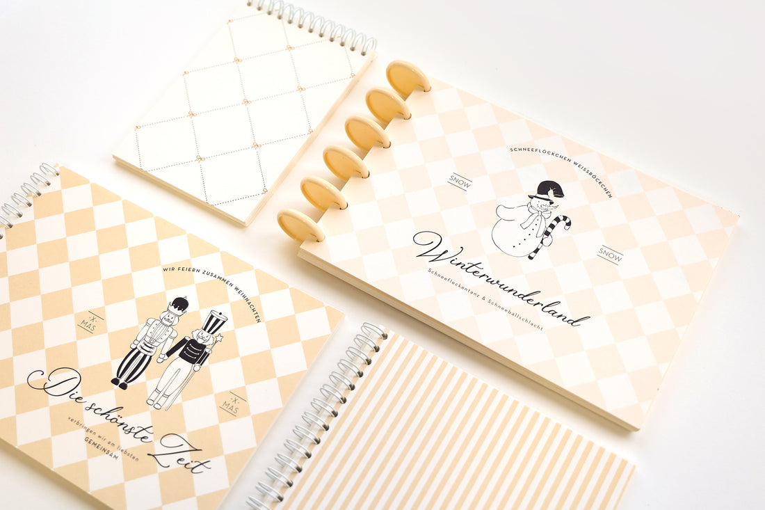 Vier spiral- und scheibengebundene Notizbücher mit beige-weißem Muster und verspielten Illustrationen zum Thema Winter.
