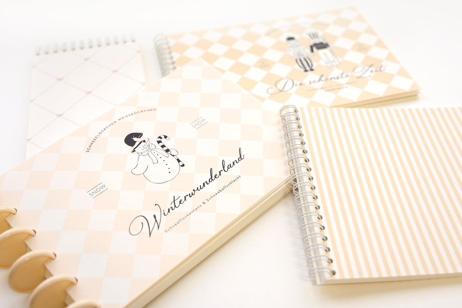 Vier pastellfarbene Notizbücher mit geometrischen Mustern und winterlichen Illustrationen auf einer weißen Oberfläche.