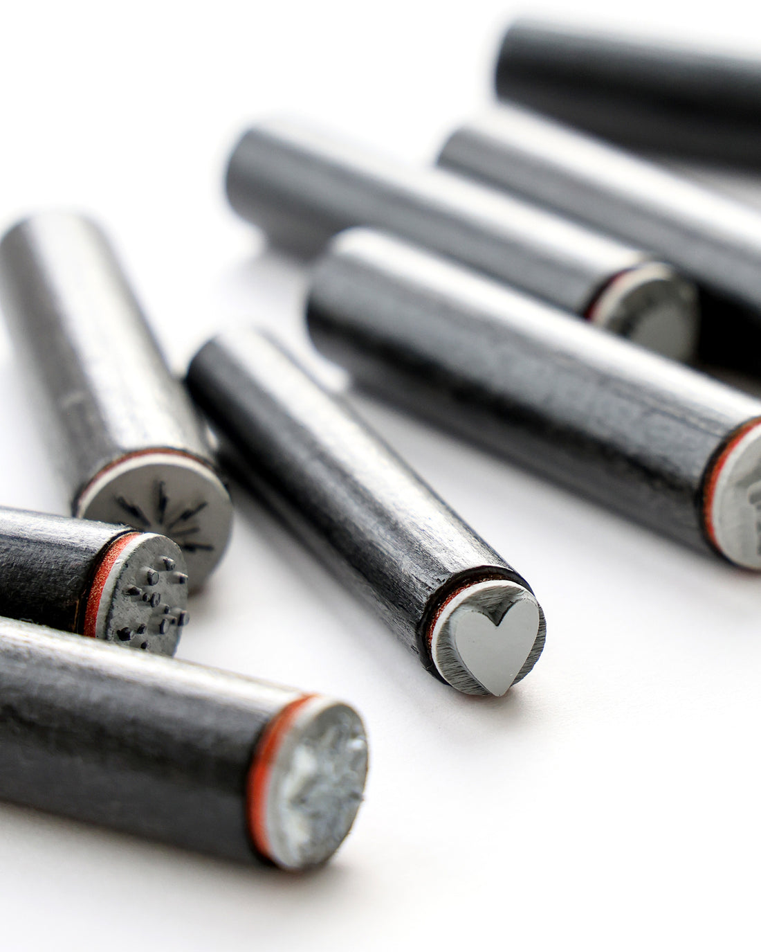 Stanzwerkzeuge aus Metall mit eingravierten Spitzen, einschließlich einer Herzform, angeordnet auf einer weißen Oberfläche.