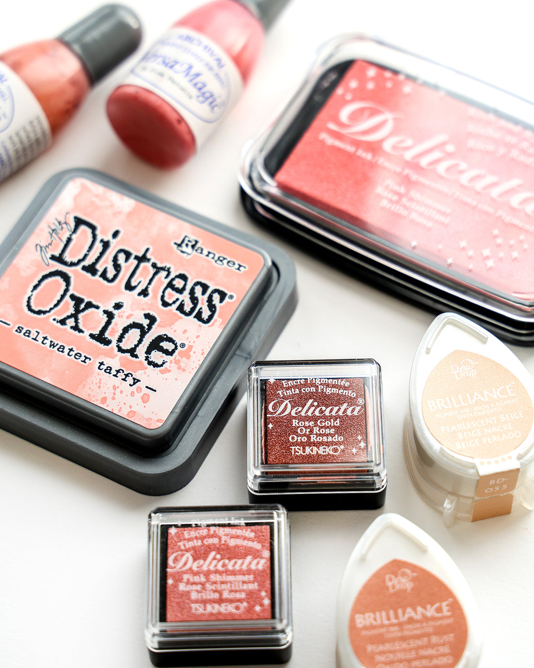 Verschiedene rosa und pfirsichfarbene Stempelkissen und Flaschen zum Stempeln und Basteln auf einer weißen Fläche.