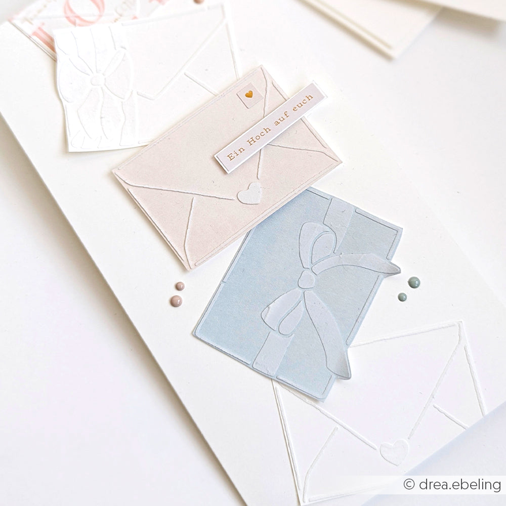 Drei pastellfarbene Briefumschläge mit Schleifen und einem deutschen Etikett auf weißer Karte, akzentuiert mit kleinen farbigen Punkten - perfekt für Stencil-Brieffreuden oder Schablonen-Papierprojekte mit wiederverwendbaren Stencils von Alexandra Renke.