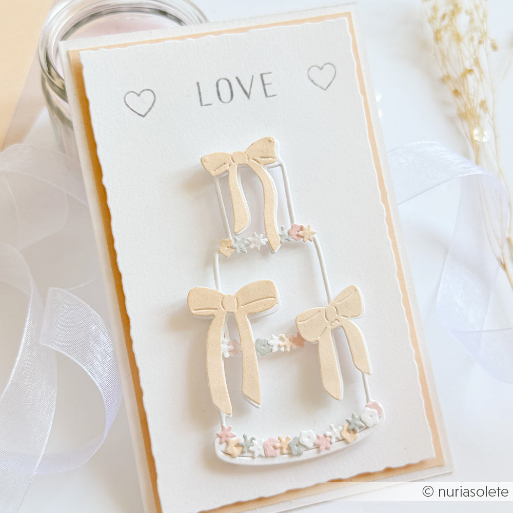 Handgefertigte Hochzeitskarte von Alexandra Renke mit einer Outline Torte mit Schleifen, pastellfarbenen Schleifen, kleinen Blumen und "LOVE" mit Herzen - hergestellt mit Motivstanze DieCut Systeme für elegante Details.
