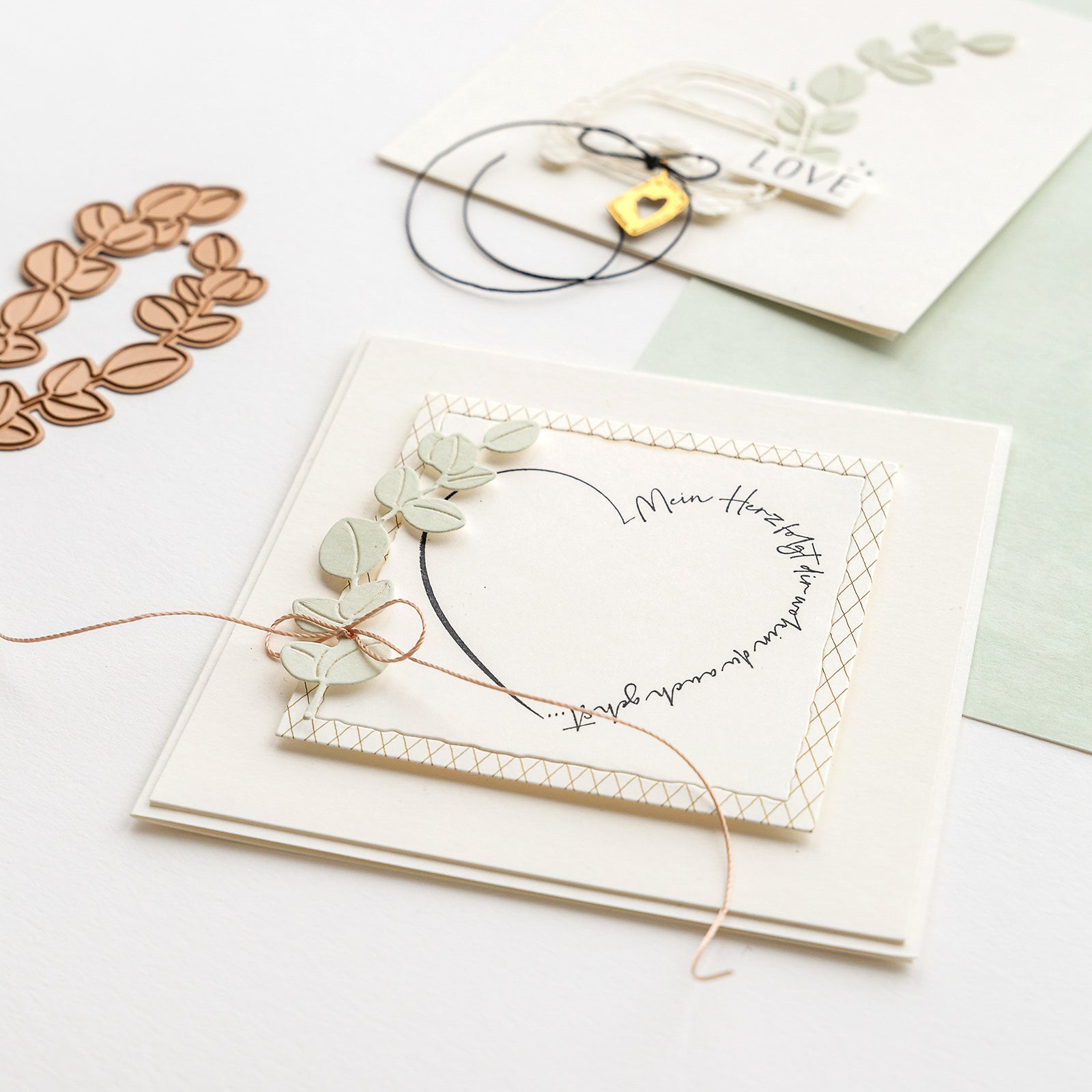 Handgefertigte Grußkarten von Alexandra Renke mit Herzmotiven, Blättern und Kordeldekorationen auf weißer Oberfläche - ideal für Papierprojekte oder zum Gestalten mit Ihrem Lieblingsholzstempel.
