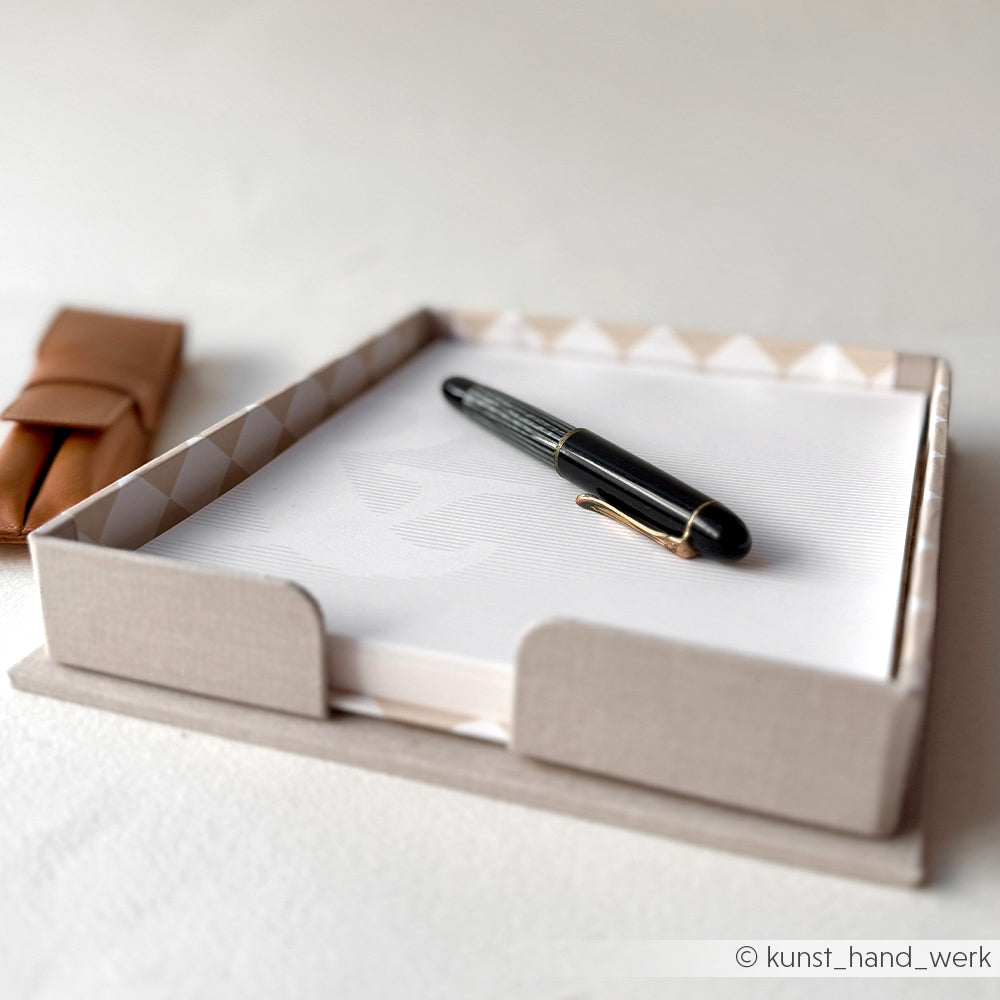 Schwarzer Füllfederhalter von Alexandra Renke auf weißem Papier in einem beigen Zettelbox-Halter, im Hintergrund ein Graupappe Zuschnitte-Etui.