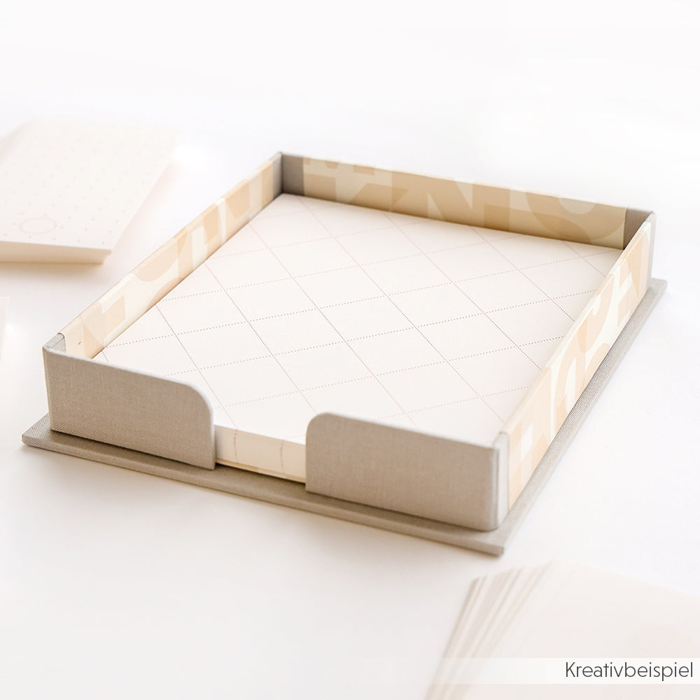 Ein beiges Zettelbox-Tablett von Alexandra Renke hält einen Stapel gemusterter Papierbögen auf einem weißen Schreibtisch.