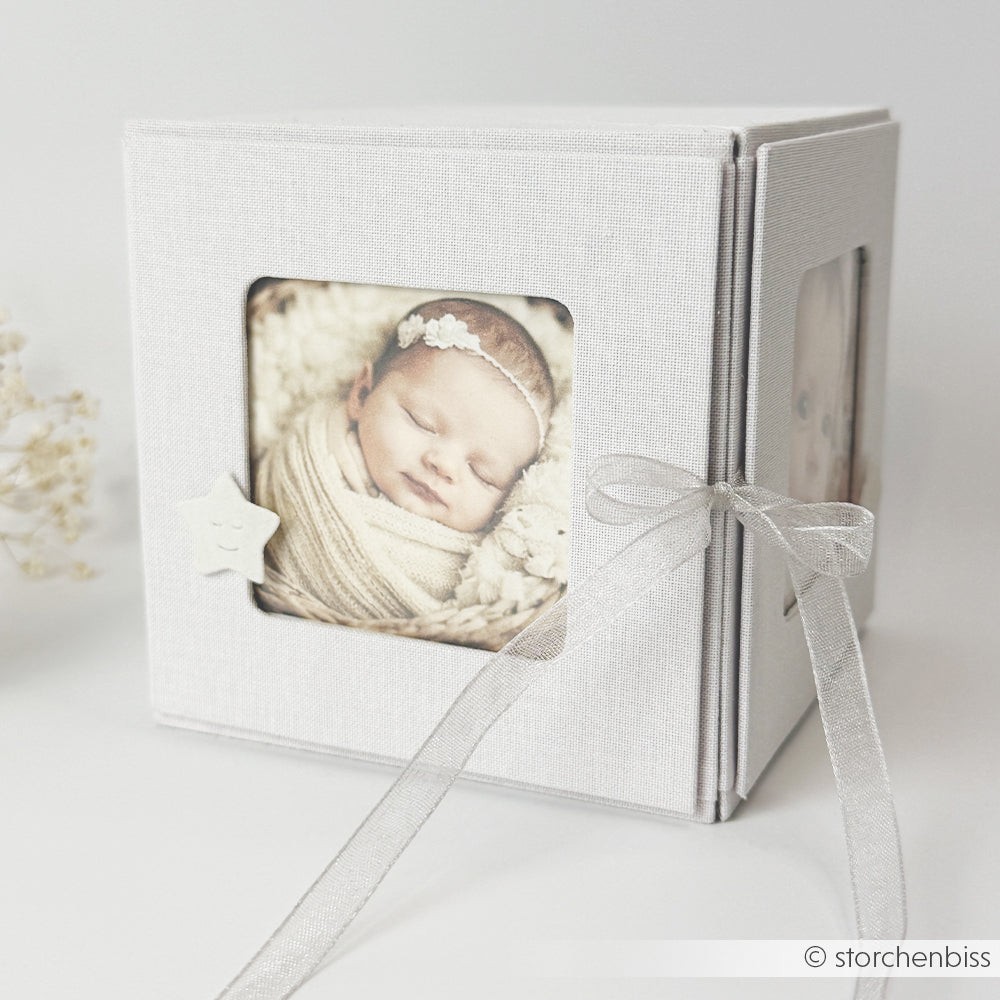 Bezaubernde weiße Fotobox von Alexandra Renke mit einem Babyfoto auf der Vorderseite, gebunden mit einem durchsichtigen Band und verziert mit einem kleinen Stern - ideal, um wertvolle Erinnerungen festzuhalten und zu verschenken.