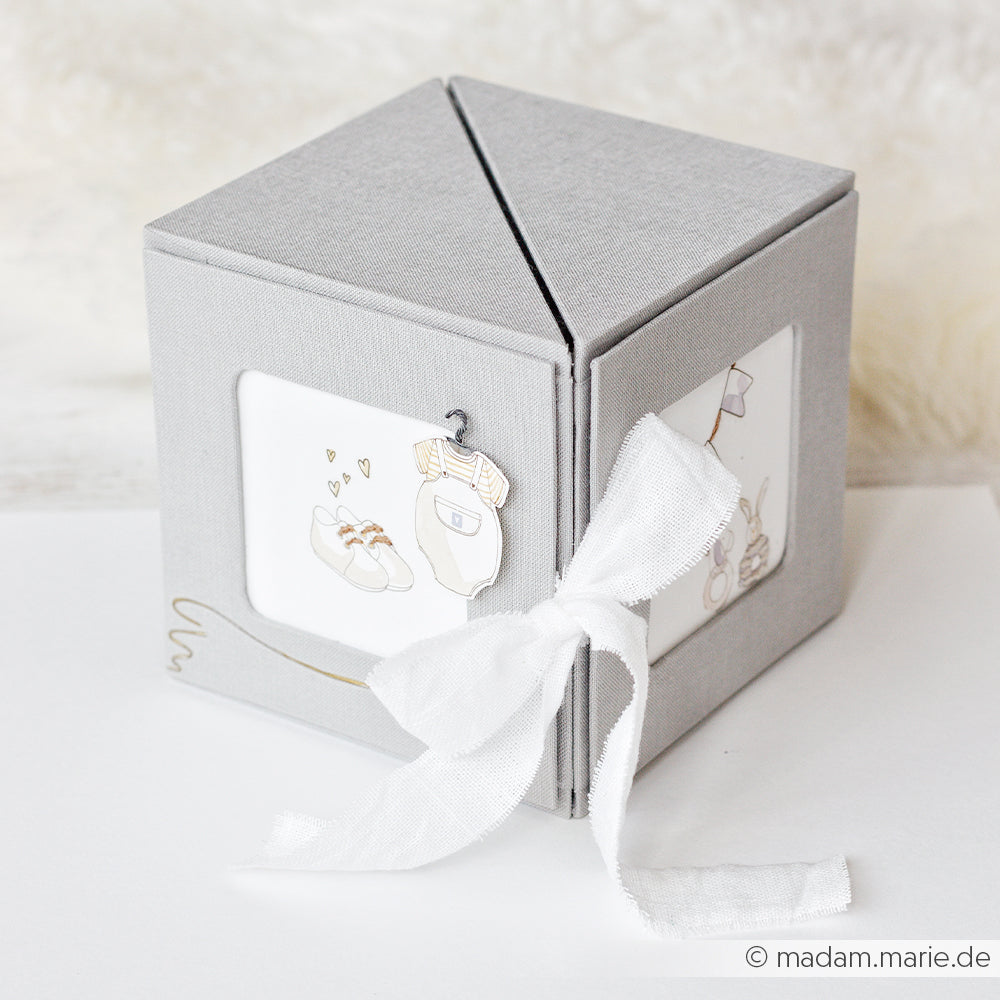 Graue, würfelförmige Alexandra Renke PAPPKit-Geschenkbox mit weißer Schleife und Dekoration im Babymotiv - eine elegante Fotowürfelbox zur Aufbewahrung wertvoller Erinnerungen.