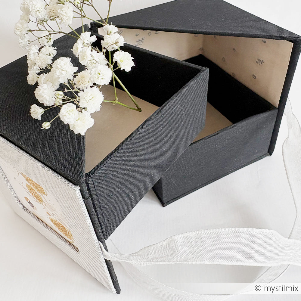 Schwarz-weiße Geschenkbox mit Schleife, teilweise geöffnet, enthält weiße Blumen - diese elegante Alexandra Renke Fotobox verleiht jedem Anlass einen Hauch von Charme.