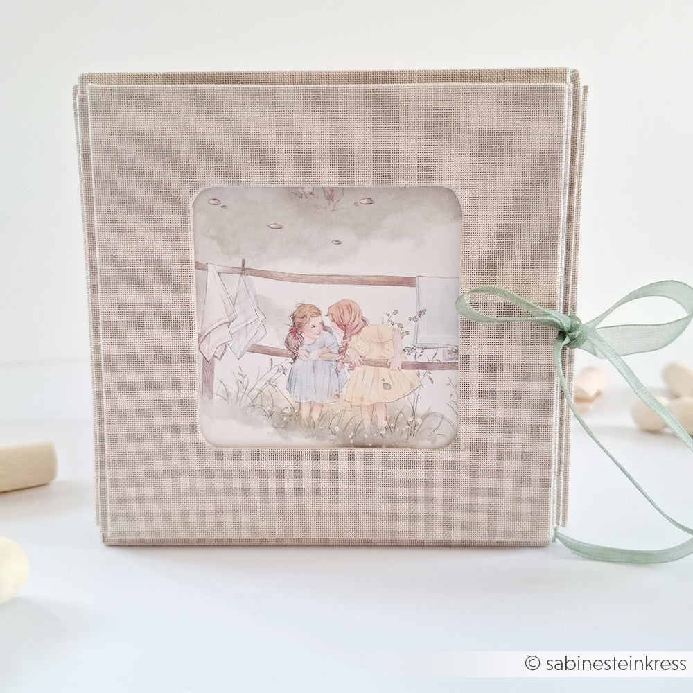 Quadratisches beigefarbenes Fotoalbum von Alexandra Renke mit einem PAPPKit-Fenster mit einer Illustration von zwei Mädchen, die im Freien stehen.