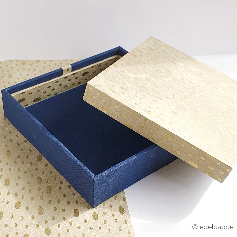 Eine blaue Alexandra Renke PAPPKit-Schachtel mit goldfarbenem Deckel, teilweise geöffnet und auf passendem goldfarbenem und weißem Papier - perfekt für das Verpacken von Geschenken oder das Basteln einer eigenen Schuberbox.