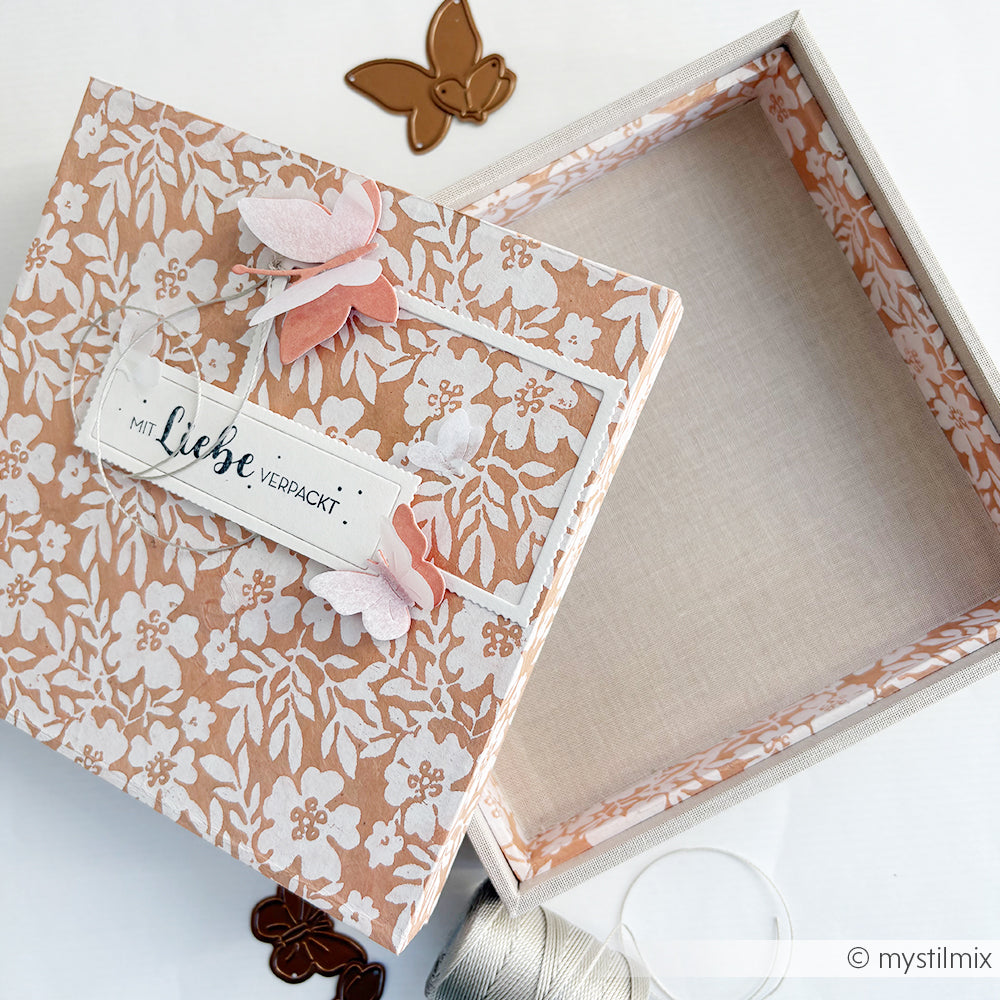 Quadratische Blumengeschenkbox von Alexandra Renke, ohne Deckel, verziert mit Papierschmetterlingen und einem "Mit Liebe verpackt"-Anhänger - perfekt zum Selbermachen von Geschenken oder zum Basteln einer PAPPKit-Einlegerbox für besondere Anlässe.