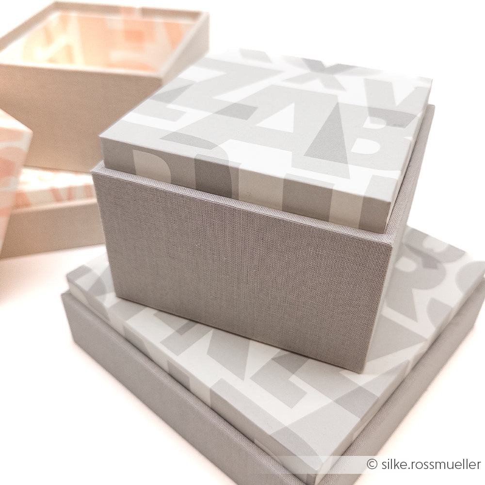 Gestapelte grau-weiß gemusterte Alexandra Renke Geschenkboxen, eine offen, auf weißem Hintergrund - eine tolle Inspiration für Geschenkverpackungen selbst machen oder DIY-Projekte mit dem Alexandra Renke PAPPKit Einsteckbox Bastelset.