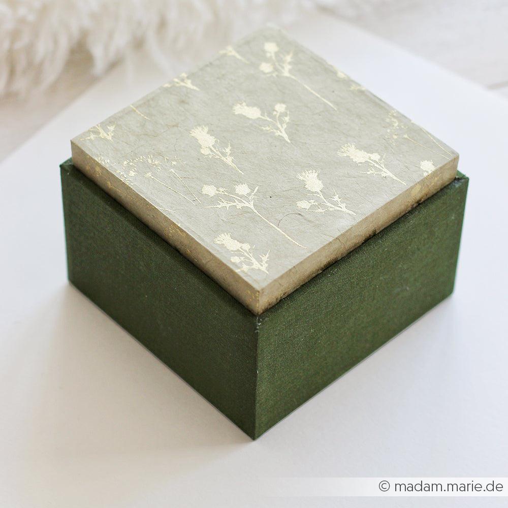 Eine quadratische grüne Einsteckbox von Alexandra Renke mit einem floral gemusterten Deckel, der auf einer weißen Fläche steht - ideal für ausgefallene Geschenkverpackungen.