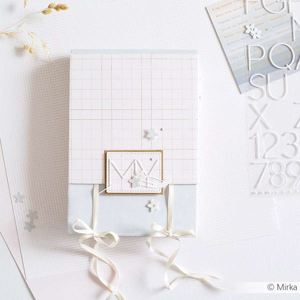 Eine pastellfarbene Geschenkbox mit Bändern, Gittermuster, kleinen Verzierungen und einem 3D-Effekt-Alpha-Sticker von Alexandra Renke auf weißem, strukturiertem Hintergrund.