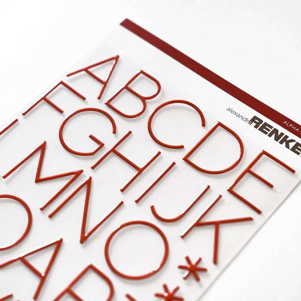 Rote Alpha-Sticker-Buchstaben mit 3D-Effekt sind auf einem weißen Blatt angeordnet und tragen in der rechten oberen Ecke den Markennamen Alexandra Renke.
