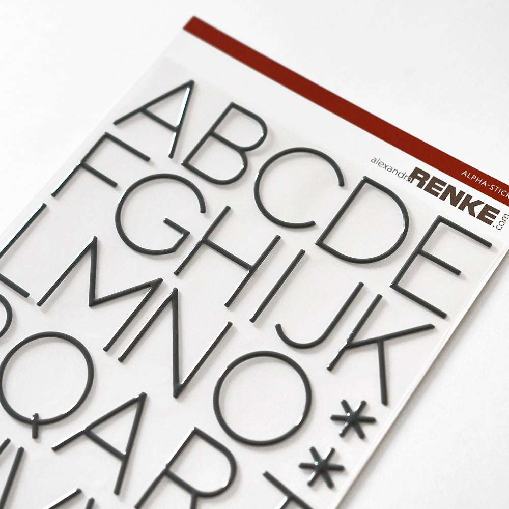 Alexandra Renke Alpha Sticker Alphabet-Sticker in Diamantgrau, präsentiert auf einem weißen Blatt mit einem rot-weißen Etikett am oberen Rand.