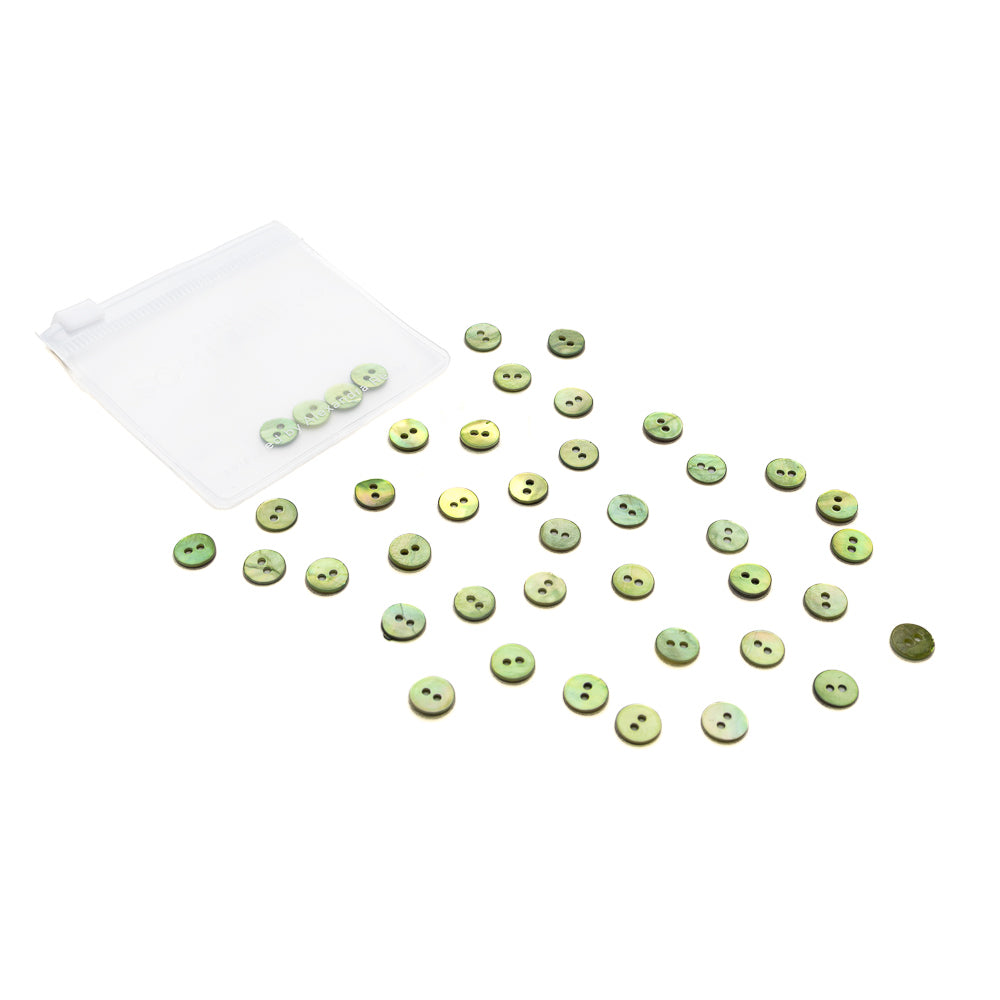 Kleine grüne Alexandra Renke Muschelknöpfe sind auf einer weißen Fläche verstreut, einige befinden sich in einem transparenten Ziplock-Beutel.