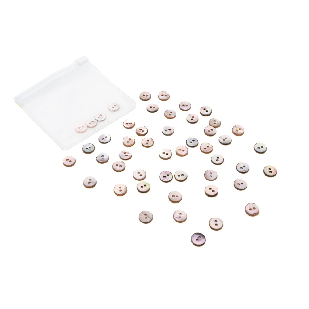 Ein kleiner weißer Beutel von Alexandra Renke mit rosa Akoya Muschelknöpfen, die auf weißem Hintergrund verstreut sind.