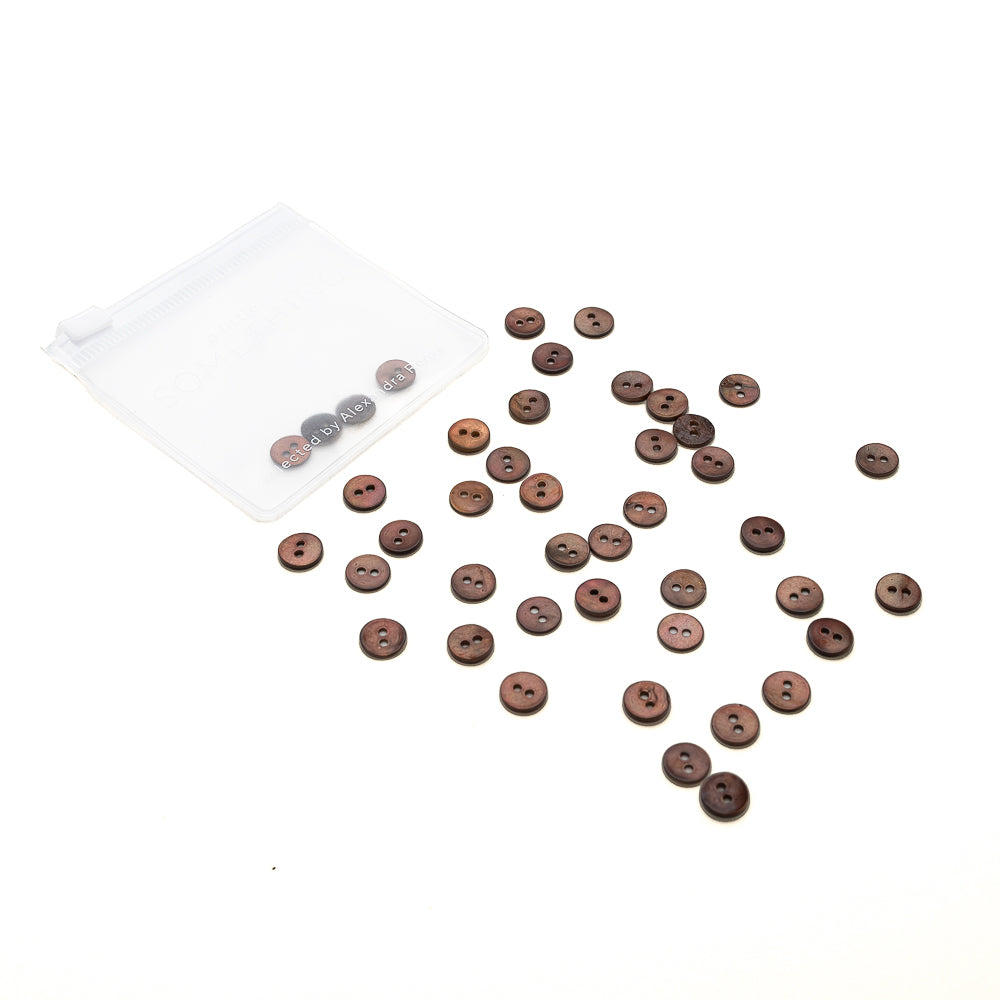 Alexandra Renke kleine braune Muschelknöpfe sind neben einem transparenten Plastikbeutel auf weißem Hintergrund verstreut.